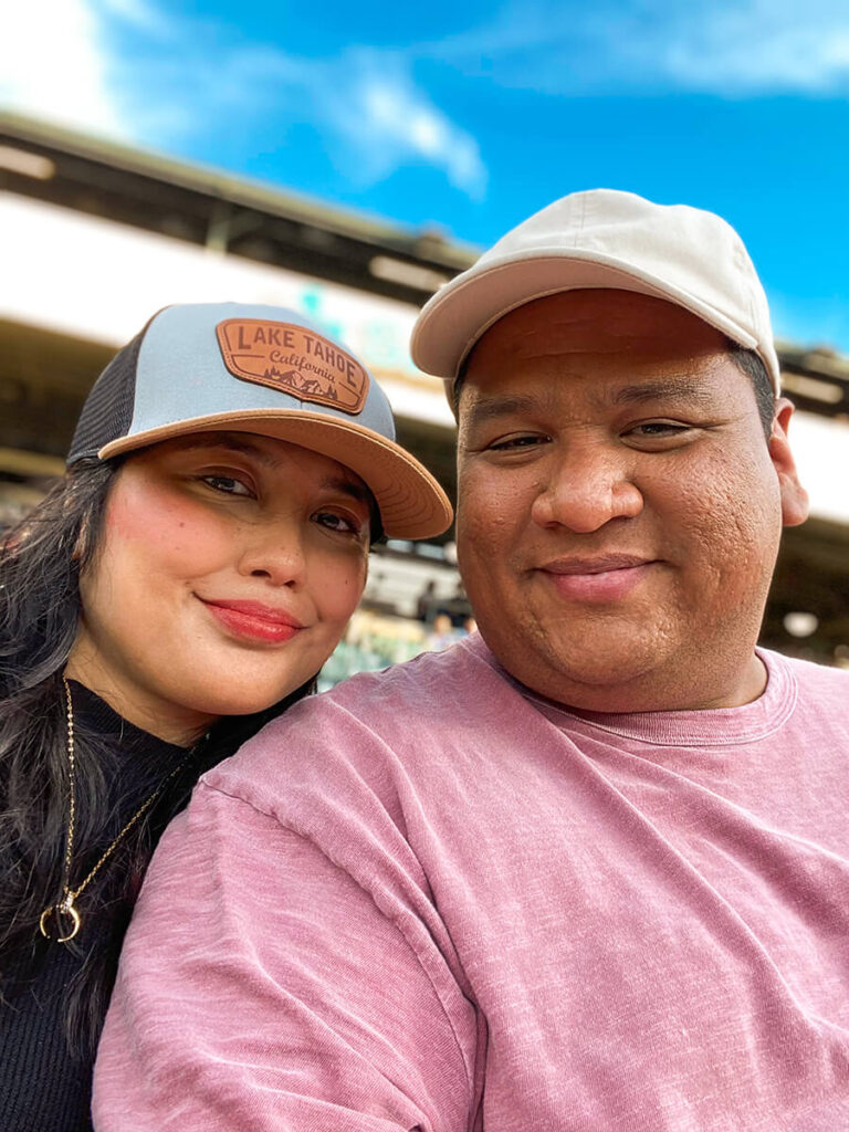 Hannah and Cecilio taking a selfie sitting at a seat in Sutter Health Park, watching a Sacramento River Cats game 